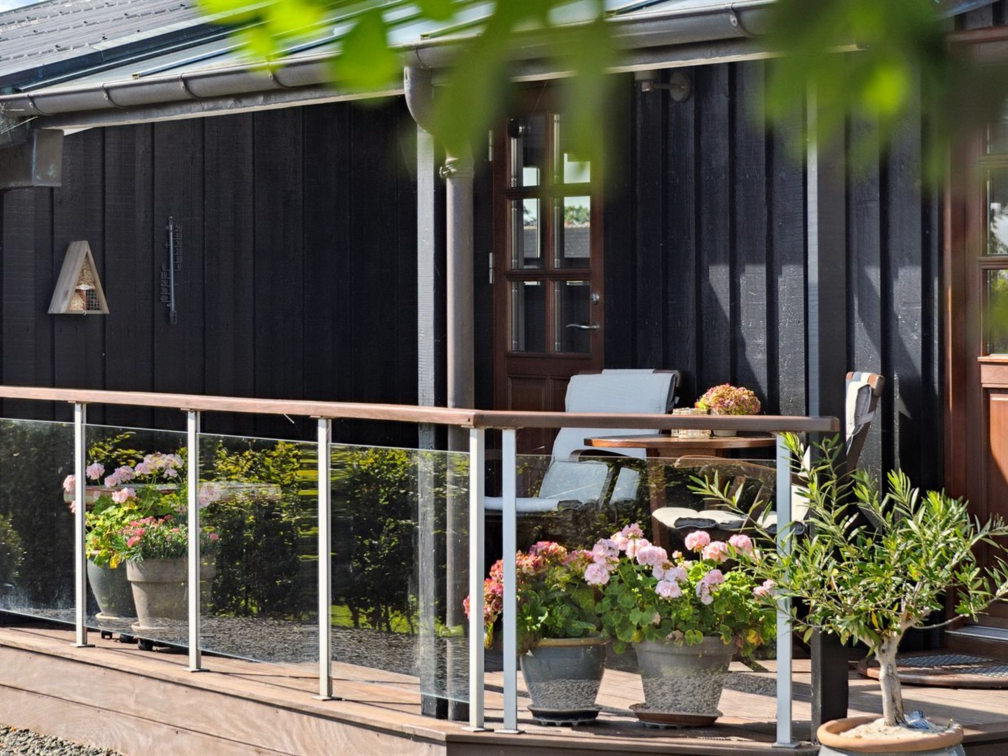 A wooden house with a balcony, potted plants, and a chair.