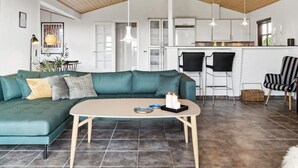 Una sala de estar moderna con un sofá color turquesa, techo de madera y una cocina con armarios blancos y una barra.