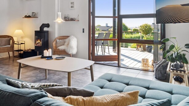 Una sala de estar acogedora con un sofá, una mesa, una chimenea y un amplio ventanal corredera que da a un patio exterior.
