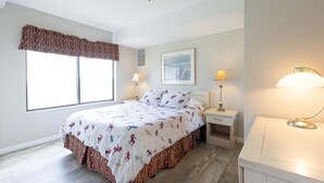 A bedroom with a large bed, two bedside tables with lamps, a window with a valance, and a framed picture on the wall.