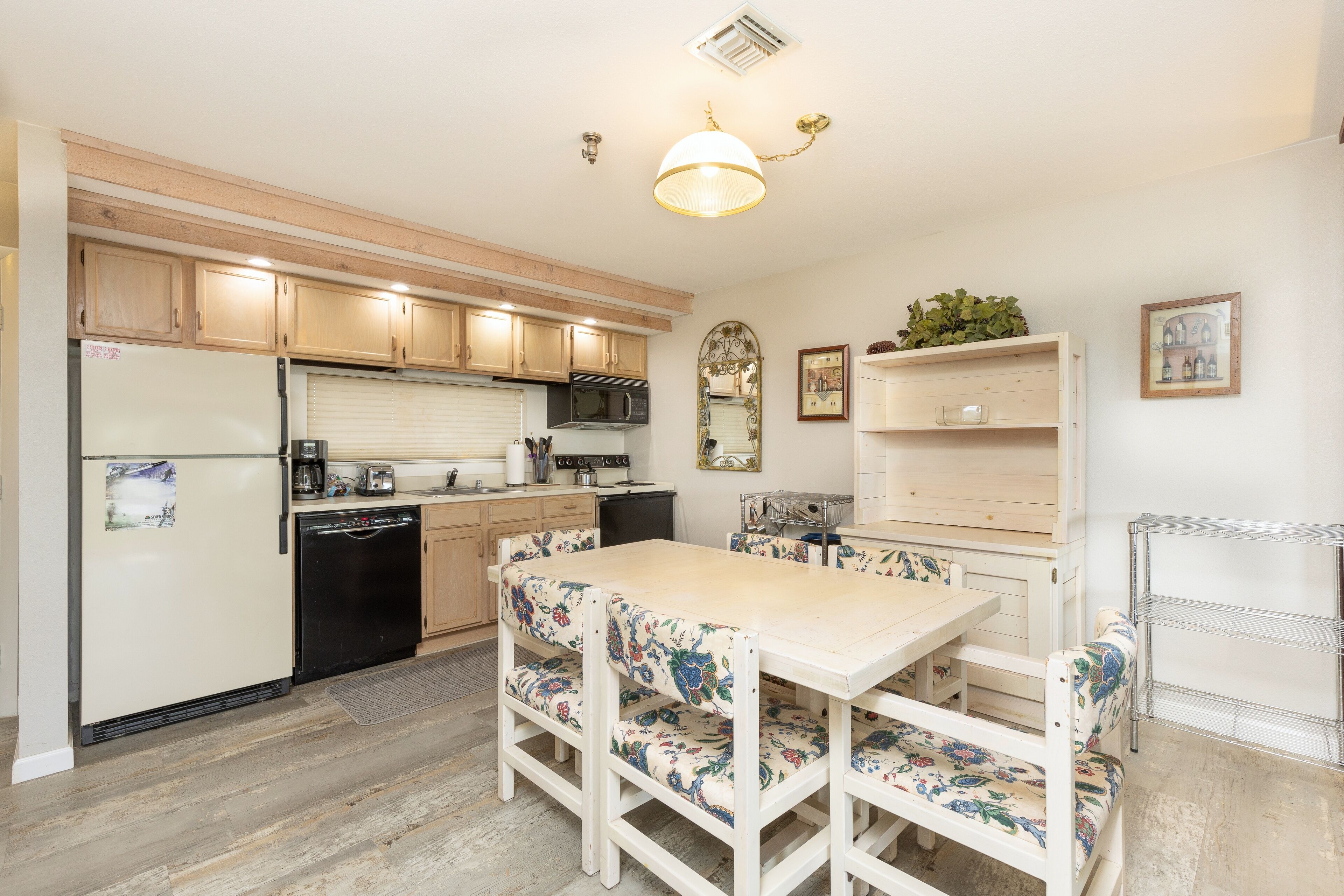 A kitchen with wooden cabinets, a refrigerator, a microwave, and a dining table with floral chairs.