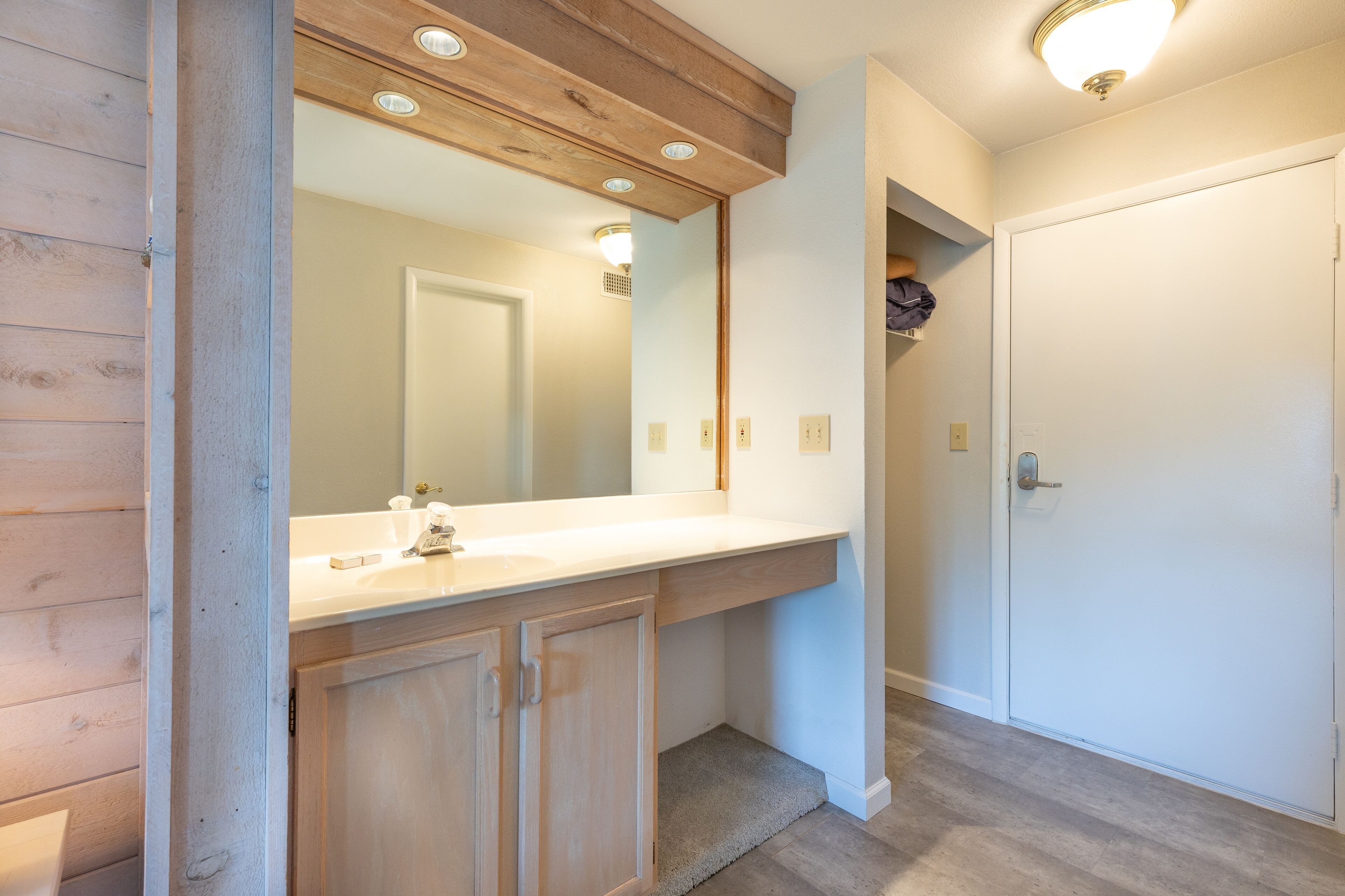 A bathroom with wooden cabinetry, a white sink, and a large mirror.