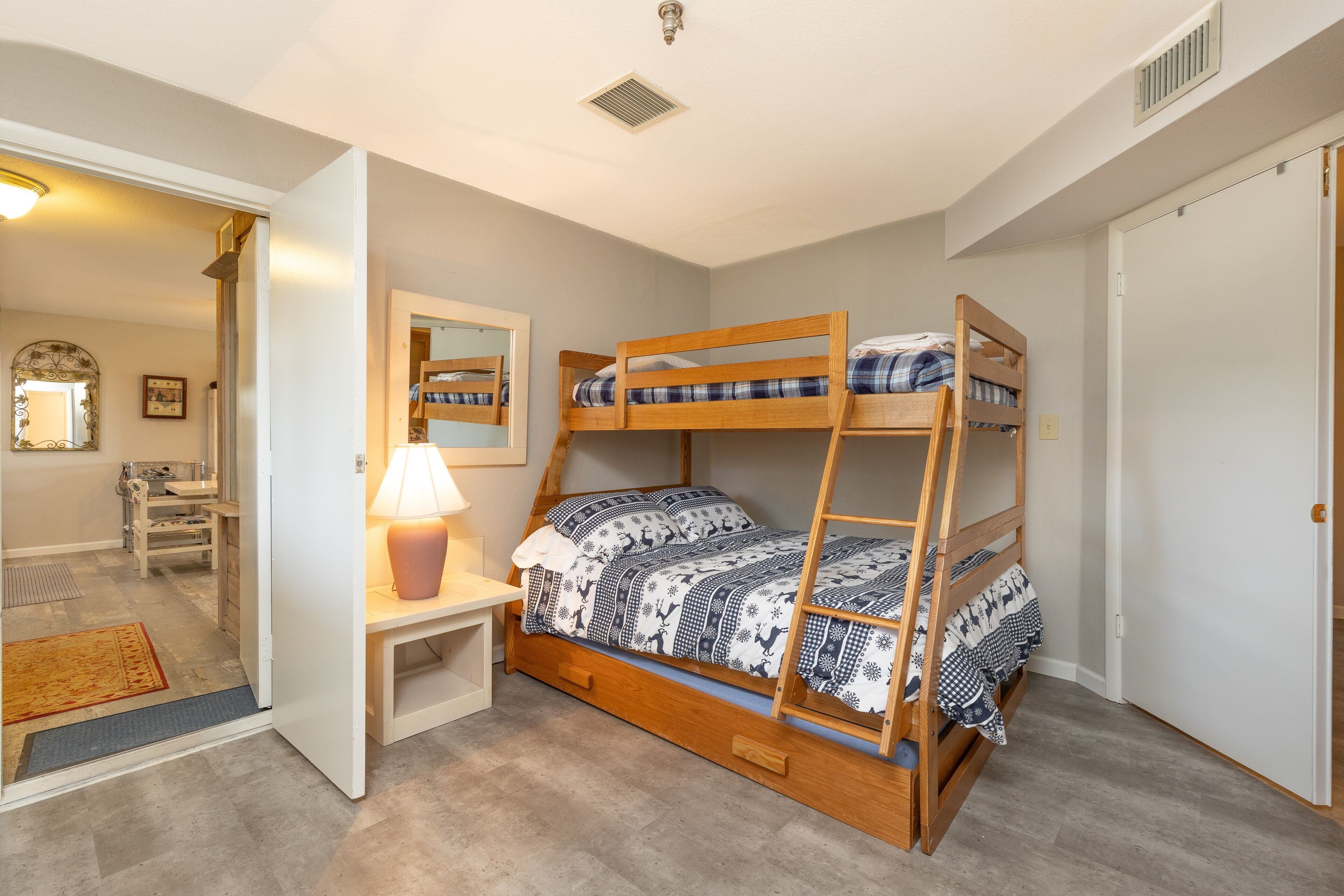 Una cama litera con estructura de madera y ropa de cama estampada, una mesita de noche con lámpara y un espejo en la pared.