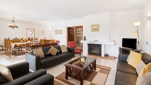 A living room with a sofa, coffee table, TV, fireplace, dining area, and chandelier. - Casa das Areias with Private Pool, Wi-Fi, and Air Conditioning (Porches)