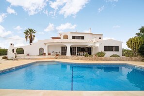 Une villa blanche dotée d’une piscine, de murs en pierre et d’un patio aménagé avec du mobilier d’extérieur.