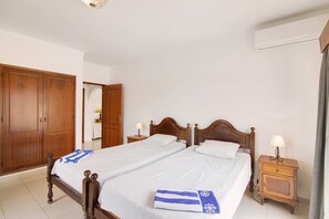 Cama doble con cabecera de madera, dos mesitas de noche con lámparas, un armario y un aire acondicionado instalado en la pared.