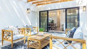 An outdoor patio with wooden furniture, including sofas and a coffee table, and a glass door leading to an interior dining area.