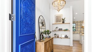 A hallway with a blue door, a wooden console table with decorative items, a chandelier, and a patterned wall.