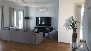 A modern living room with a grey sofa, a flat-screen TV, a ceiling fan, and a large window with curtains.