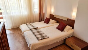 A double bed with a plaid blanket and two red pillows, wooden nightstands, and a wooden floor.