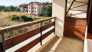 A balcony with a wooden railing, a tiled floor, and a view of buildings in the background.