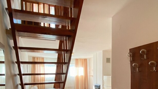 A staircase with wooden railings leading to an upper floor, a seating area with a bench and table, and a door with hooks.