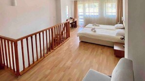 Quarto de hotel com piso de madeira, uma cama, um sofá e uma varanda com guarda-corpo de madeira.