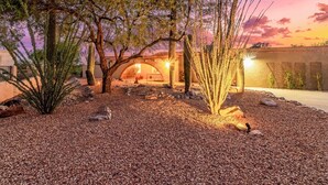 Un paysage désertique avec un bâtiment doté d’une entrée en arc de cercle, entouré de cactus et d’un sol de gravier.