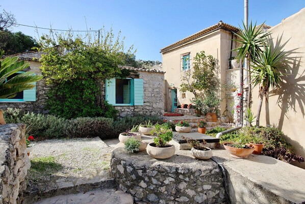 A courtyard with stone walls, potted plants, and a building with blue shutters.