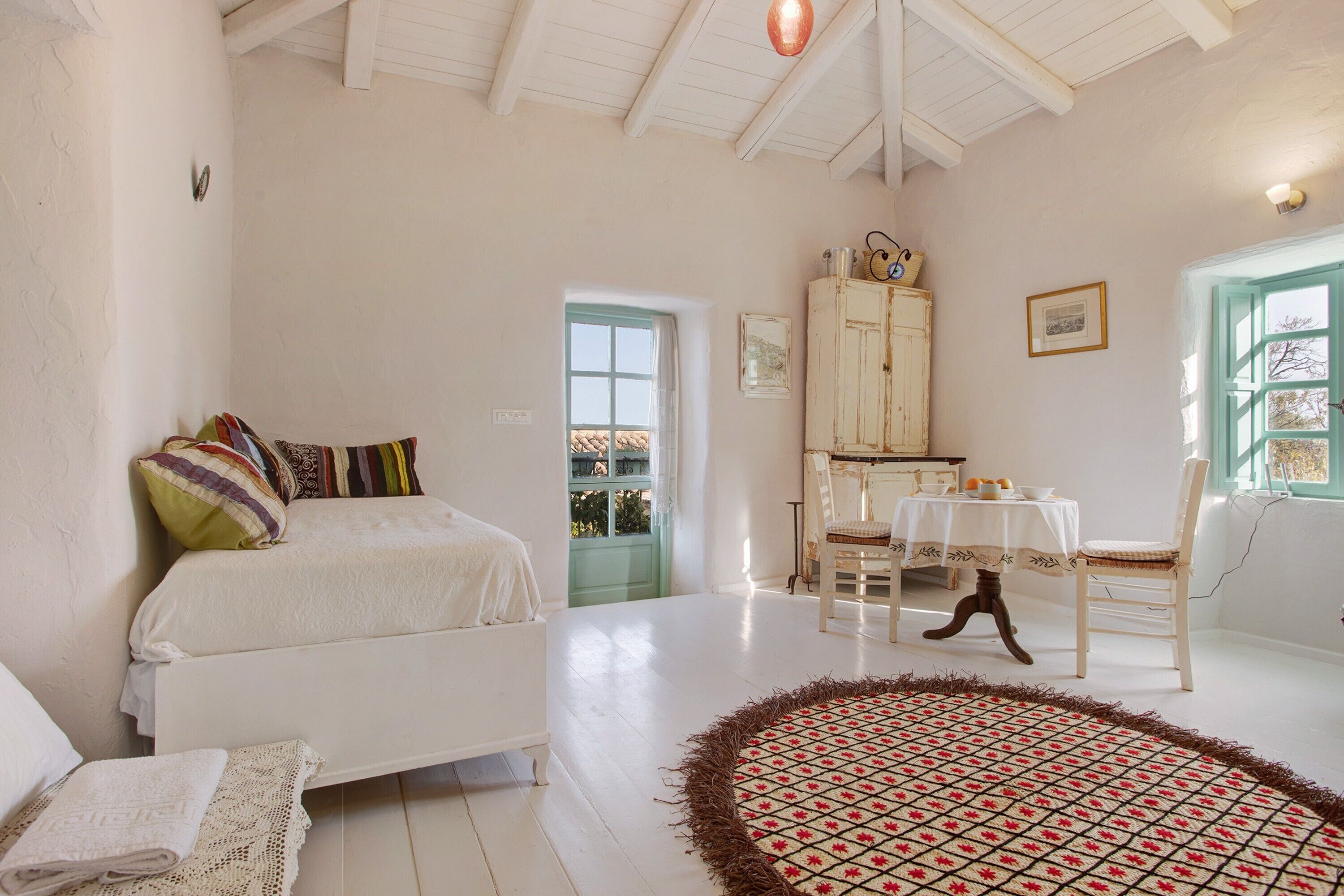 A bedroom with a bed, a round rug, a dining table with chairs, and a cabinet.