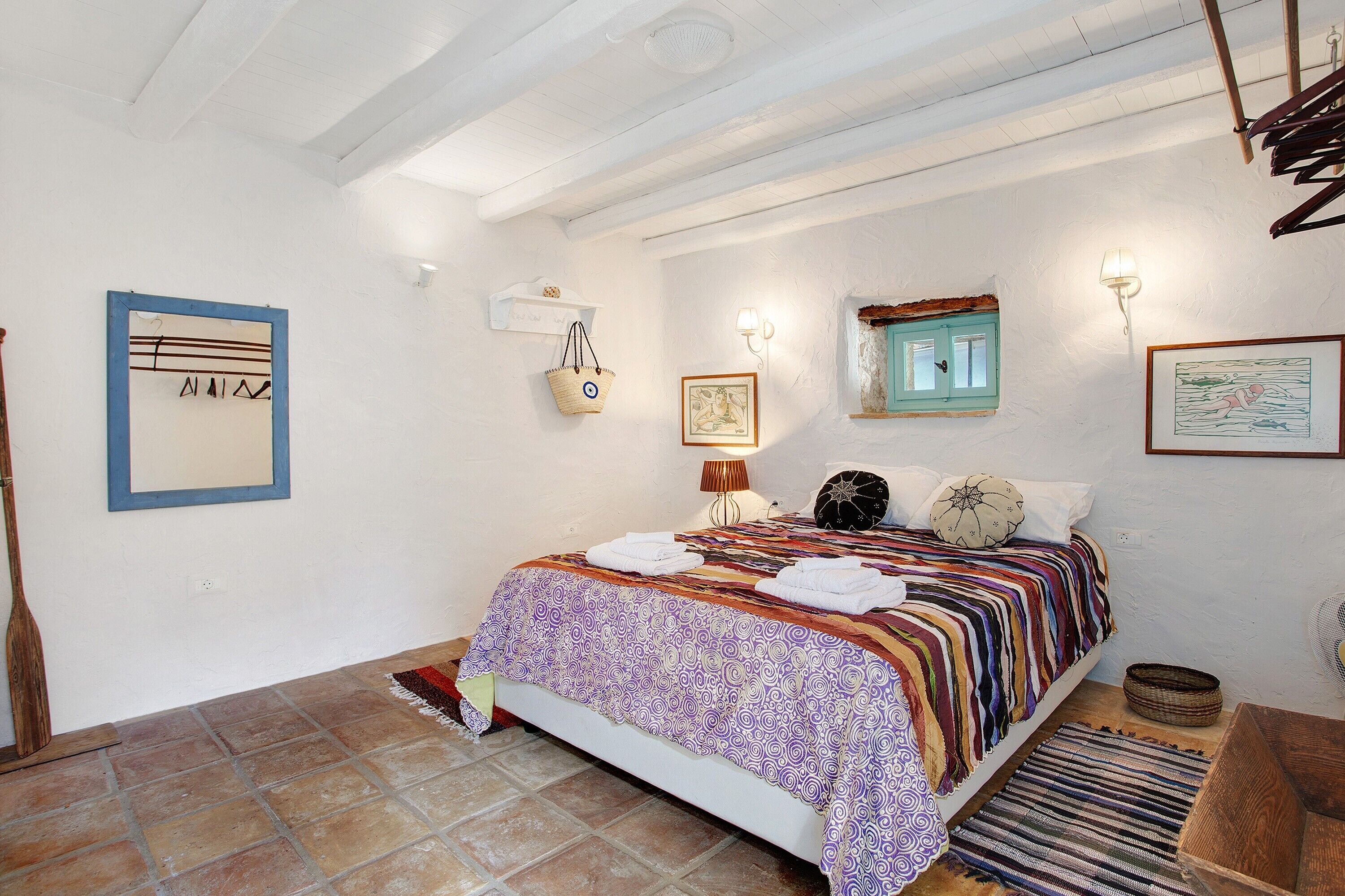 A bedroom with a bed, a wall-mounted shelf, a wall lamp, and a window with a curtain.
