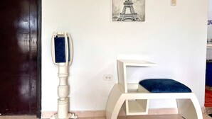 Een kamer met een witte muur, een lijst met een afbeelding van de Eiffeltoren, een witte krabboom en een donker houten deur.