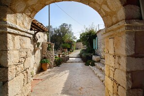 A stone pathway leading through an archway, flanked by stone walls and potted plants.