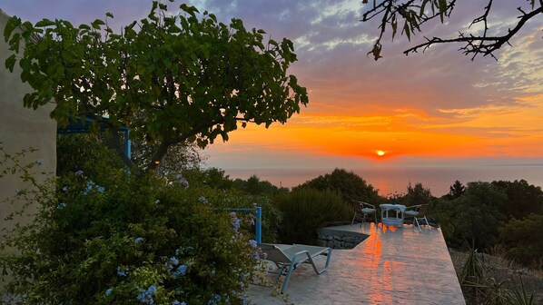 A sunset view from a terrace with outdoor seating and a view of the sea.