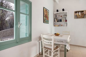 Ein Essbereich mit Tisch und Stühlen, ein Fenster mit Blick auf Bäume und ein Regal mit verschiedenen Gegenständen.