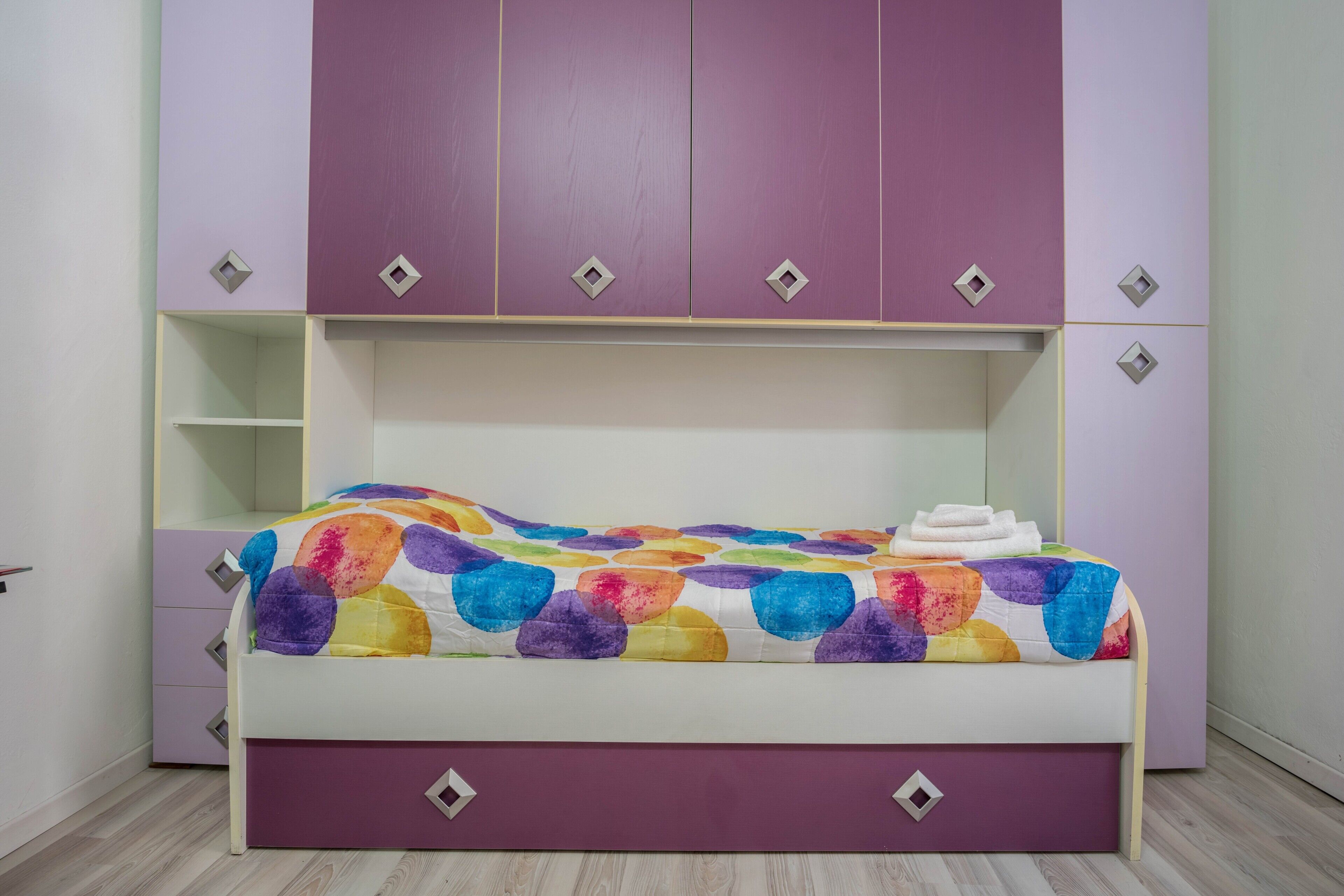 A bedroom with a bed, purple wardrobe, and a colorful bedspread.