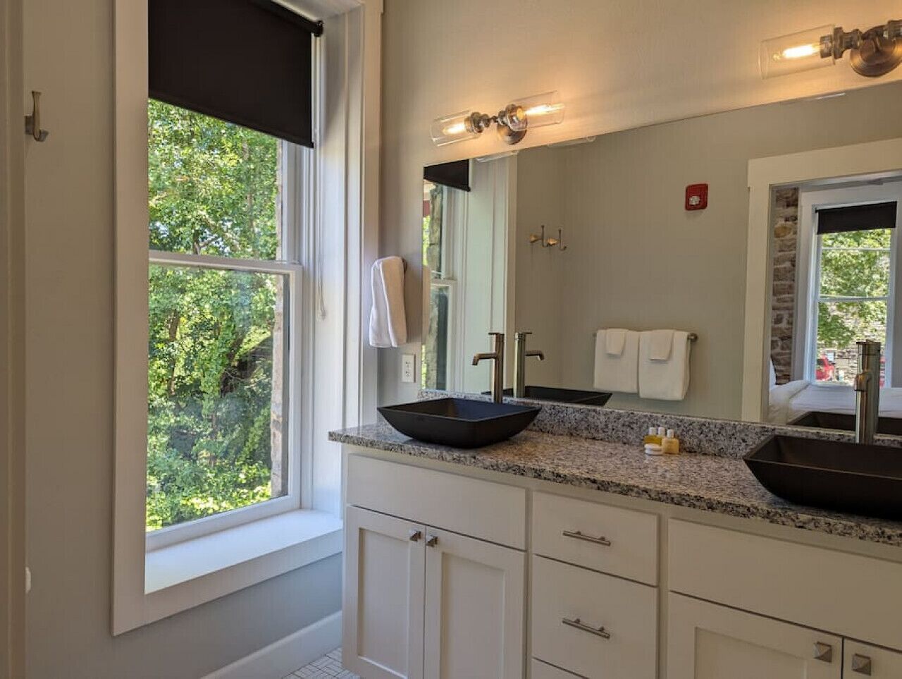 A bathroom with two sinks, a large mirror, and a window with a view of trees.
