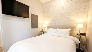 Hotellihuone, jossa on suuri sänky, kaksi yöpöytää valaisimineen, seinälle asennettu litteänäyttöinen televisio ja puinen sängynpääty.