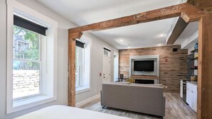 A modern bedroom with a large bed, a TV in the living area, and a kitchen in the background. - Downtown+HotTub+Wifi+FreeParking @151 Spring Ste A (Eureka Springs)