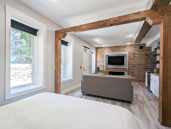 A modern bedroom with a large bed, a TV in the living area, and a kitchen in the background. - Downtown+HotTub+Wifi+FreeParking @151 Spring Ste A (Eureka Springs)