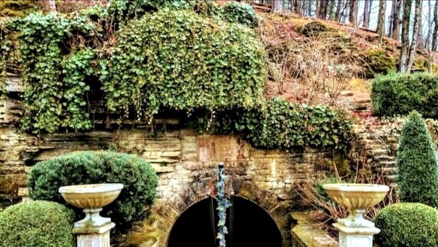 A stone archway with a circular opening, flanked by two stone urns and surrounded by neatly trimmed hedges. - Downtown+HotTub+Wifi+FreeParking @151 Spring Ste F (Eureka Springs)