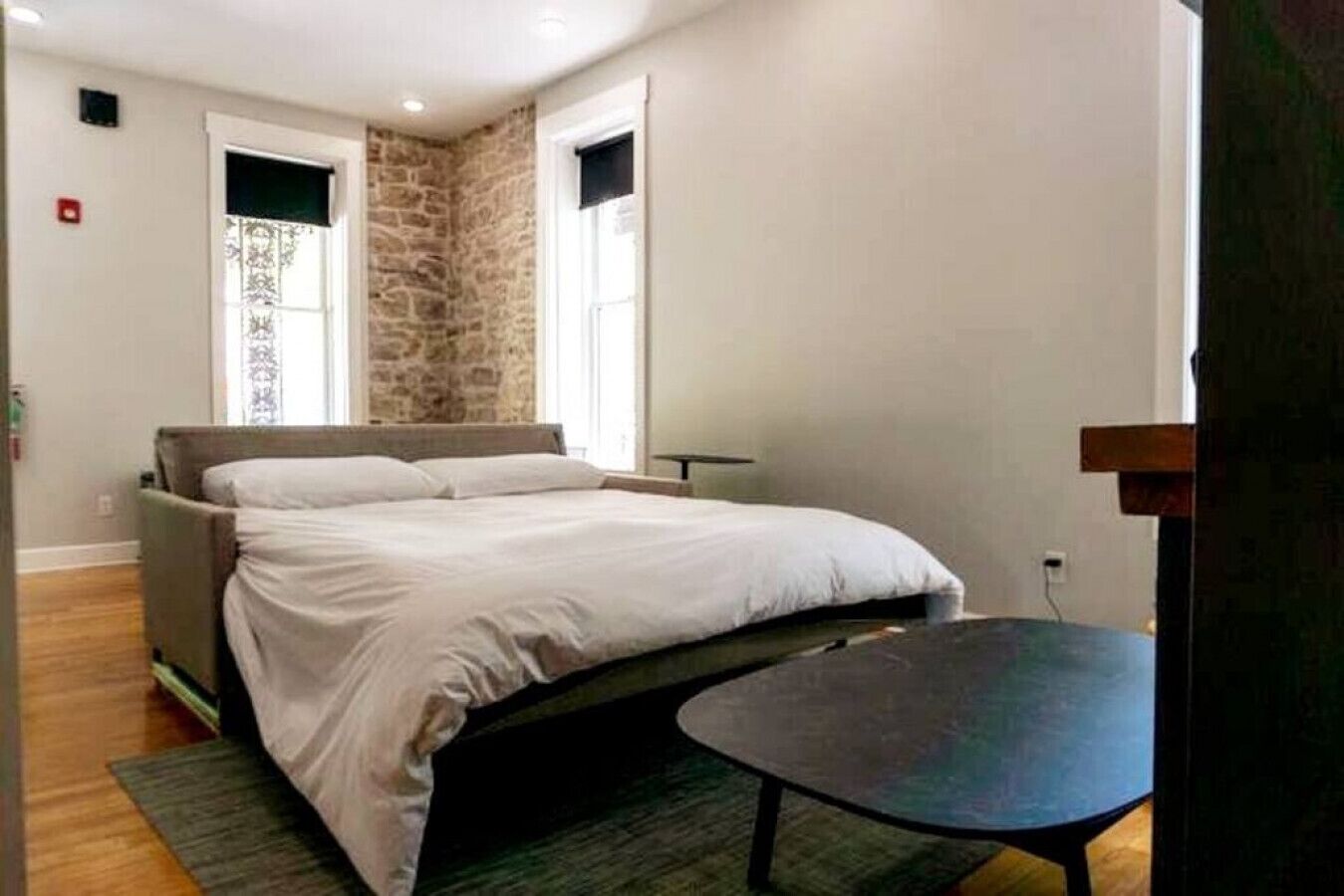 A bedroom with a bed, a small table, and a stone accent wall.