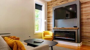 Ein modernes Wohnzimmer mit Kamin, einem an einer Holzwand montierten Flachbildfernseher, einer Couch, einem gelben Sessel und einem Couchtisch.