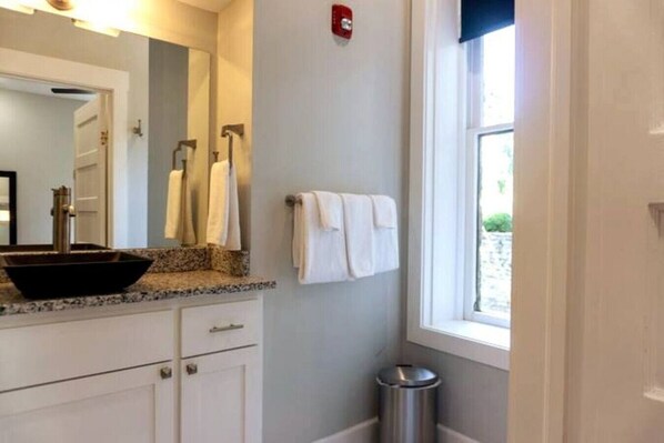 A bathroom with a vessel sink, a mirror, a towel rack, and a window.