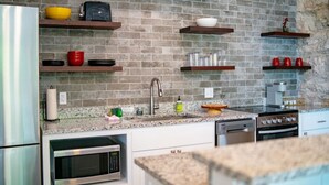 A modern kitchen with granite countertops, stainless steel appliances, and wooden shelves holding various kitchen items. - Downtown+HotTub+Wifi+FreeParking @151 Spring Ste C (Eureka Springs)