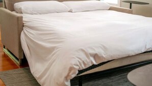 A bed with white bedding in a room with a grey sofa and a small round table. - Downtown+HotTub+Wifi+FreeParking @151 Spring Ste C (Eureka Springs)