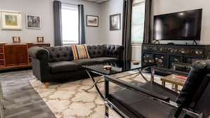 Un salon avec un canapé noir, une table basse en verre, un téléviseur et un meuble en bois.