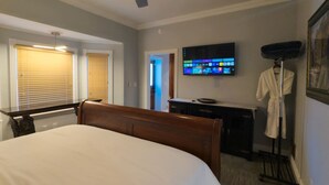 A hotel room with a large bed, a desk, a television, and a robe rack. - Downtown Villa 2 at Sweet Spring Wifi Free Parking (Eureka Springs)