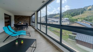Ein geräumiger Balkon mit Blick auf eine hügelige Landschaft, ein Essbereich mit Tisch und Stühlen sowie eine Lounge-Ecke mit Liegestühlen.