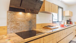 Eine moderne Küche mit Holzausstattung, einer Edelstahl-Dunstabzugshaube und einer großen Kochinsel mit Schneidebrett und Wasserkocher.
