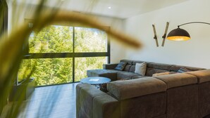 Ein modernes Wohnzimmer mit großem Fenster, einer Couch, einem runden Couchtisch und einer ungewöhnlichen Wandleuchte.