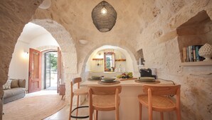 A rustic interior with a stone archway, a wooden dining table with chairs, and a hanging light fixture. - TD Trulli Altura With Pool Stunning Sunsets (Martina Franca)