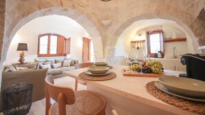 A rustic interior with stone arches, a dining area with a table set for two, and a kitchen in the background. - TD Trulli Altura With Pool Stunning Sunsets (Martina Franca)