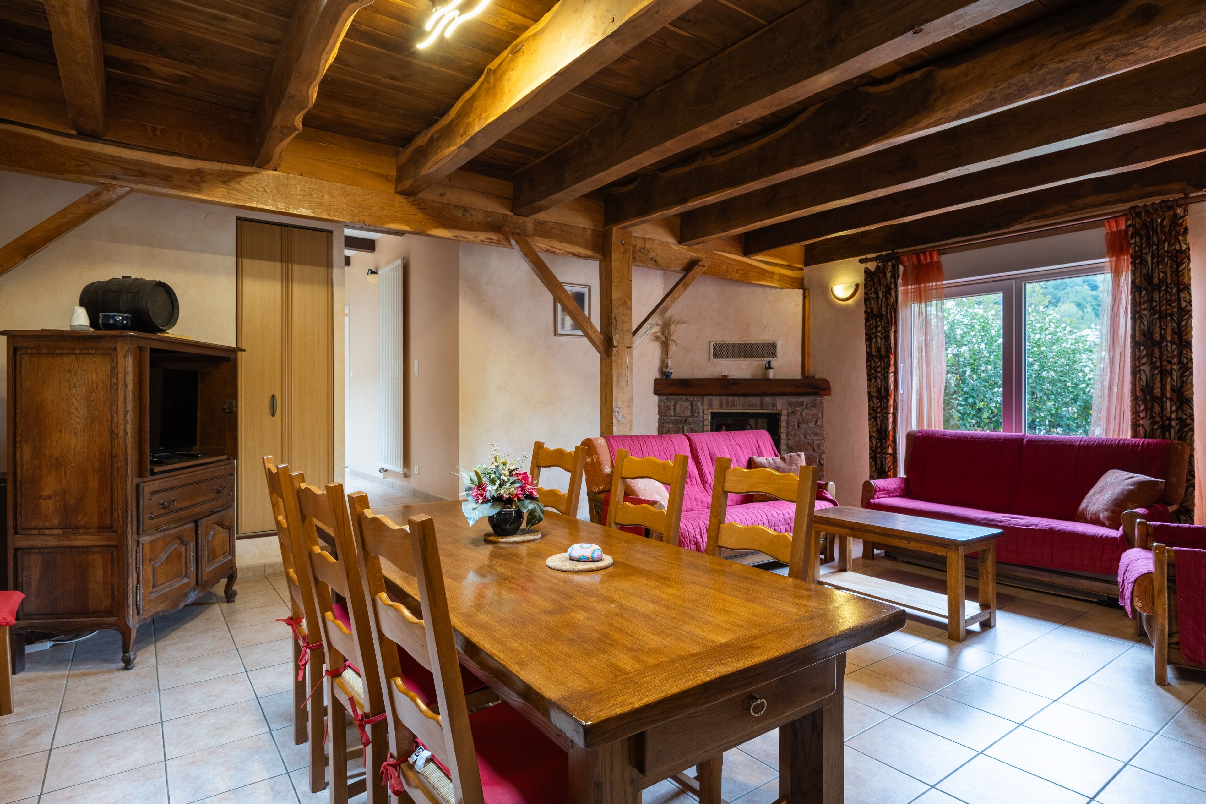 A wooden dining table with chairs, a sofa, and a fireplace in a room with exposed wooden beams.