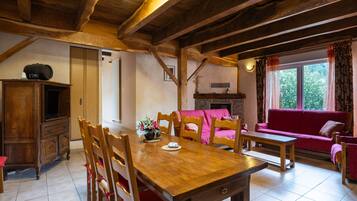 A wooden dining table with chairs, a sofa, and a fireplace in a room with exposed wooden beams.
