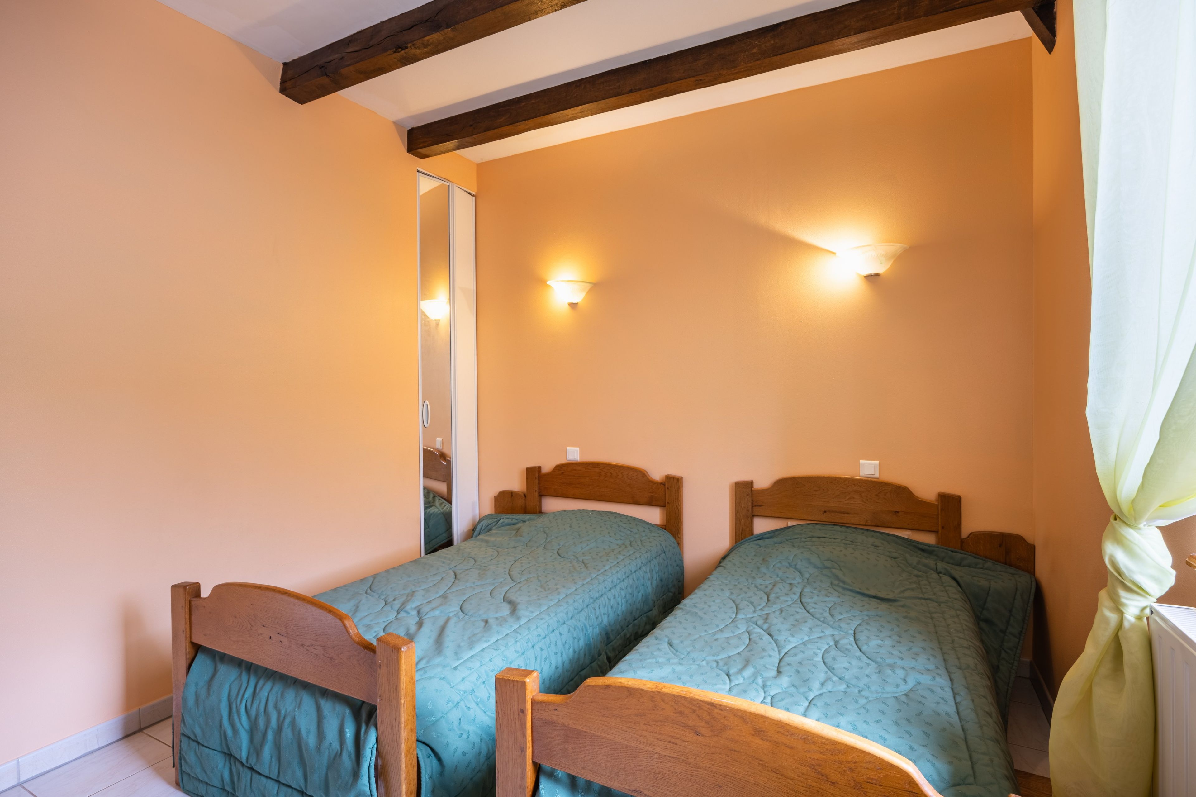 Une chambre avec deux lits en bois, un miroir et des lampes fixées au mur.