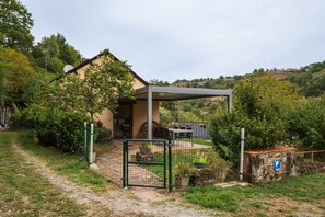 Une maison dotée d’un patio couvert, d’un jardin clôturé et d’un mur en pierre sur lequel est apposé un panneau bleu indiquant un espace de stationnement.