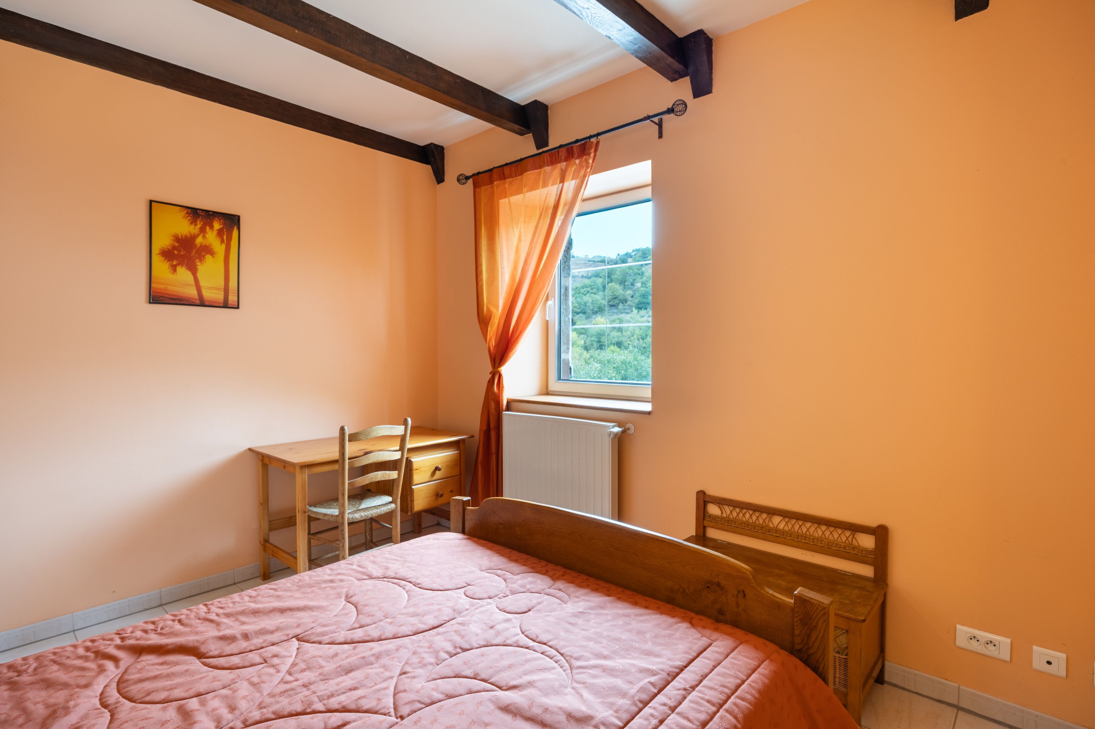 Une chambre à coucher avec un lit, un bureau et une chaise. Il y a une fenêtre avec des rideaux.