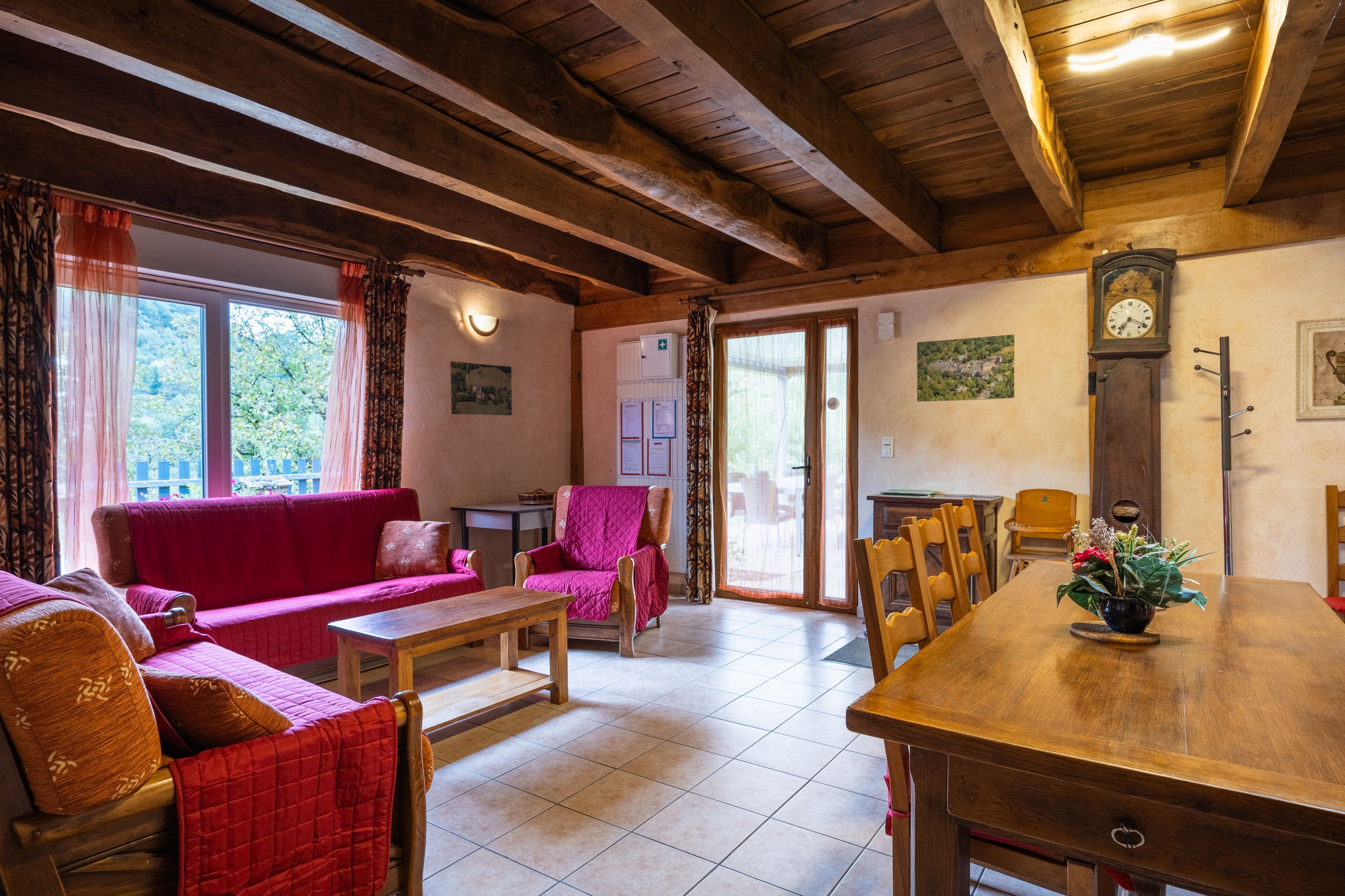 A cozy living room with a wooden ceiling, a red sofa, a wooden dining table, and a chair.