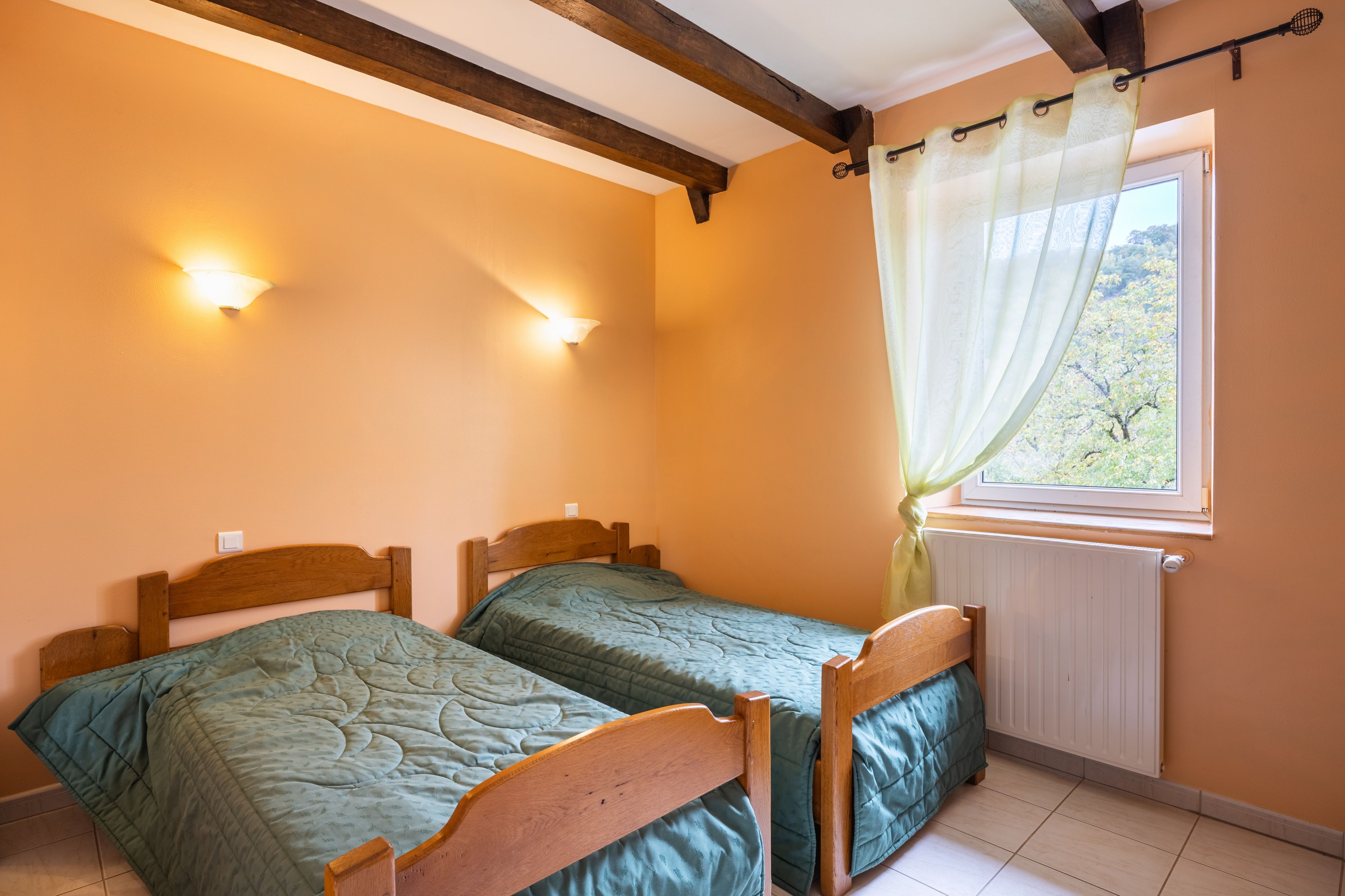 A room with two wooden beds, a window with a curtain, and wall-mounted lights.